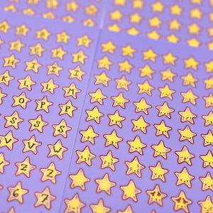 May include: Sheets of purple stickers featuring yellow star shapes with smiling faces and letters of the alphabet. The stickers have a red outline. Some stickers have numbers. The stickers are arranged in rows and columns.