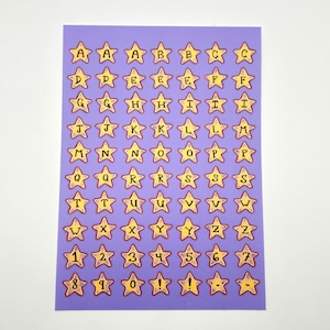 May include: A sheet of purple star-shaped stickers with yellow borders. Each star contains a letter of the alphabet or a number, from A to Z and 0 to 9, plus exclamation points. The stickers are arranged in a grid pattern.
