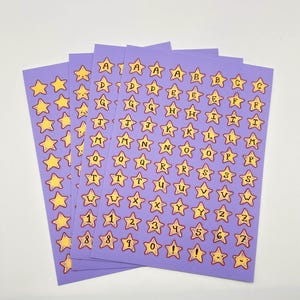 May include: Sheets of purple star-shaped stickers with yellow stars and black letters and numbers. The stickers include the alphabet, numbers 1-9, and an exclamation point. The stickers are on a white background.