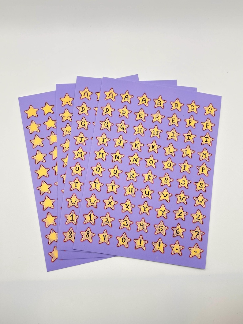 May include: Sheets of purple star-shaped stickers with yellow stars and black letters and numbers. The stickers include the alphabet, numbers 1-9, and an exclamation point. The stickers are on a white background.