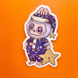 May include: A purple and blue cartoon monster wearing a nightcap and pajamas with stars and moons. The monster is holding a yellow star with a sad face.