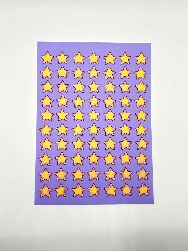 May include: A sheet of stickers with a purple background and numerous yellow star shapes with red outlines. The stars are evenly spaced across the sheet, creating a repeating pattern. The stickers are likely for crafts or decoration.
