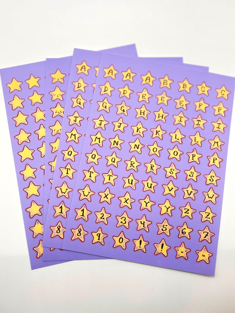 May include: Sheets of purple star-shaped stickers with yellow stars and black lettering. Each sticker features a letter of the alphabet or a number. The stickers are arranged in rows and columns, with a variety of letters and numbers.