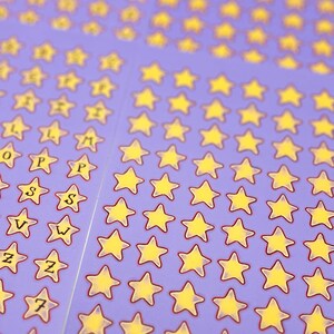May include: Sheets of purple star stickers with yellow stars and red outlines. Some stickers have letters and numbers. The stickers are arranged in neat rows and columns, creating a visually appealing pattern.
