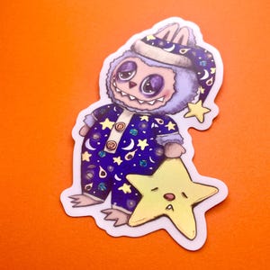 May include: A purple and blue fuzzy monster wearing a blue and white nightcap with stars and planets printed on it. The monster is holding a yellow star with a sleepy face.