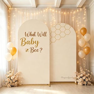 Puede incluir: Dos paneles de fondo arqueados en color crema, uno con el texto dorado What Will Baby Bee? y un icono de abeja, y el otro con un patrón de panal dorado. Decorado con racimos de globos crema y dorados y arreglos florales en color beige.