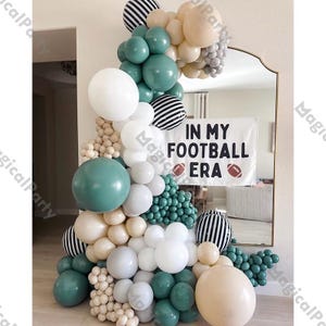 May include: A green, white, beige, and black balloon arch with a banner that reads "In My Football Era" with football icons.