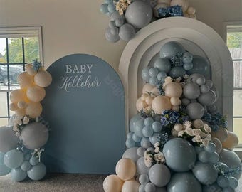 Könnte beinhalten: Ein blauer und weißer Ballonbogen mit einer blauen Hintergrundwand, auf der "BABY Kelleher" in weißer Schrift steht. Der Bogen besteht aus verschiedenen Größen von Ballons in Blautönen und Weiß.