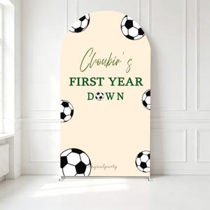 May include: An arched backdrop featuring a cream-coloured background with black and white football illustrations. The text reads "Choubin's FIRST YEAR DOWN" in dark green lettering, with the word "DOWN" incorporating a small football.