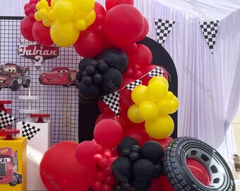 May include: Red, yellow, and black balloons arranged in an arch with a checkered flag banner. The balloons are decorated with a tire-shaped balloon and a sign that says "Fabian 2".