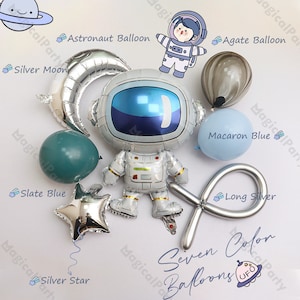 Puede incluir: Un conjunto de siete globos de diferentes colores y diseños, que incluyen una luna plateada, una estrella plateada, un globo azul pizarra, un globo azul macaron, un globo plateado largo, un globo ágata y un globo astronauta. El globo astronauta es un globo de lámina plateada con un dibujo animado de un astronauta que lleva un traje espacial blanco.