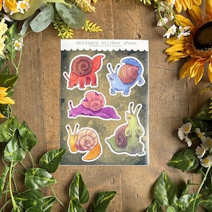 May include: A sticker sheet with six illustrated snails in vibrant colours. The snails have shells and bodies in red, blue, purple, orange, and green. The sheet is labelled "snizzard sticker sheet" with the artist's name. The background has a dark, textured pattern.