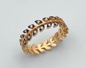 May include: A gold-colored ring featuring a leaf design. The ring is adorned with small, clear gemstones and dark accents, creating a delicate and elegant appearance. The ring's design is a continuous pattern of leaves around the band.