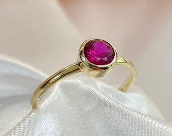 Puede incluir: Un anillo de oro con una sola piedra preciosa redonda de color rojo rubí engastada en bisel.