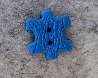 Button as puzzle piece blue black with structure in the surface, for sewing
