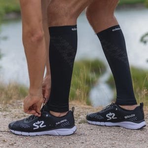 Könnte beinhalten: Schwarze Kompressionsstrümpfe und Laufschuhe. Die Strümpfe haben ein geometrisches Muster und das Wort "elev" oben. Die schwarzen Laufschuhe haben weiße Sohlen und das Wort "Route" auf der Seite. Die Marke "Salming" ist ebenfalls sichtbar.