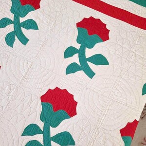 May include: A vintage quilt with a white background and a repeating pattern of red and teal flowers. The quilt is quilted with a circular pattern.