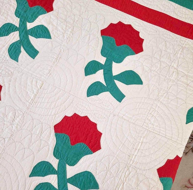 May include: A vintage quilt with a white background and a repeating pattern of red and teal flowers. The quilt is quilted with a circular pattern.