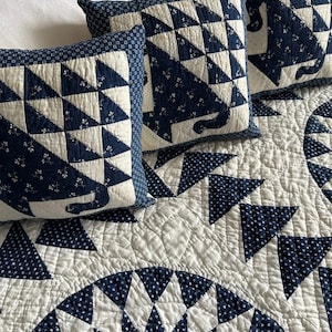 Puede incluir: Juego de cama acolchado en azul marino y blanco. El juego incluye tres almohadas cuadradas con silueta de gato y un edredón con patrones geométricos. El edredón y las almohadas están sobre una cama blanca.