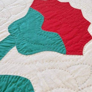 May include: A close-up of a red and green quilt block with a flower design. The quilt block is made of fabric squares sewn together with a white thread.