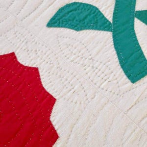 May include: Close-up of a quilt with red and green fabric squares. The quilt is stitched with white thread, creating a pattern of small, evenly spaced dots.