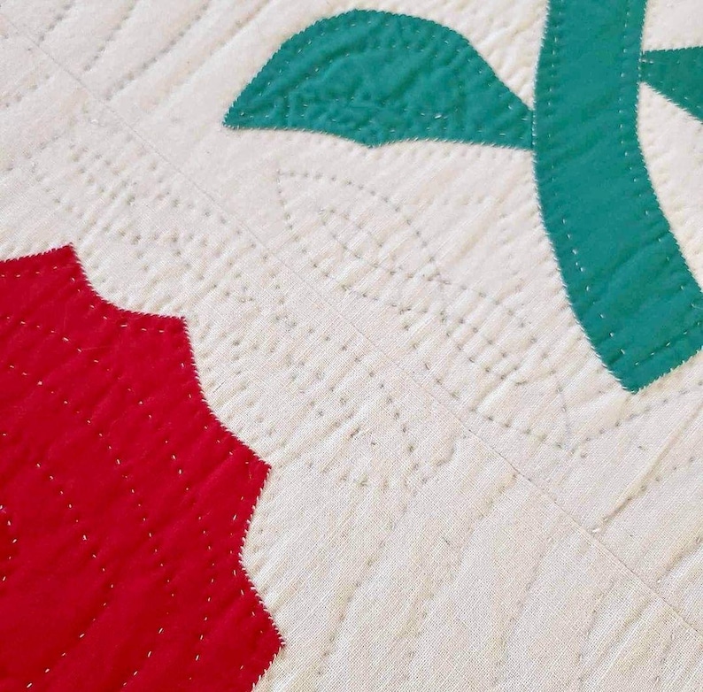 May include: Close-up of a quilt with red and green fabric squares. The quilt is stitched with white thread, creating a pattern of small, evenly spaced dots.