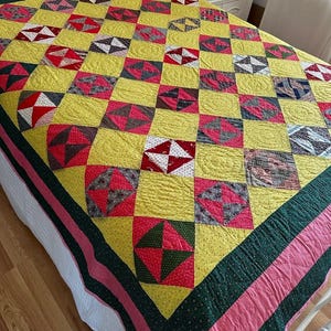 May include: A yellow, pink, and green patchwork quilt with a diamond pattern. The quilt is made of various fabrics and has a green and pink border.