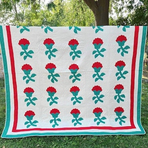 May include: A white quilt with a red and green floral pattern. The quilt has a red and green border.