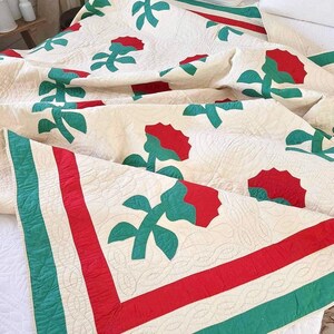 May include: A white quilt with a red and green floral pattern. The quilt has a red and green border.