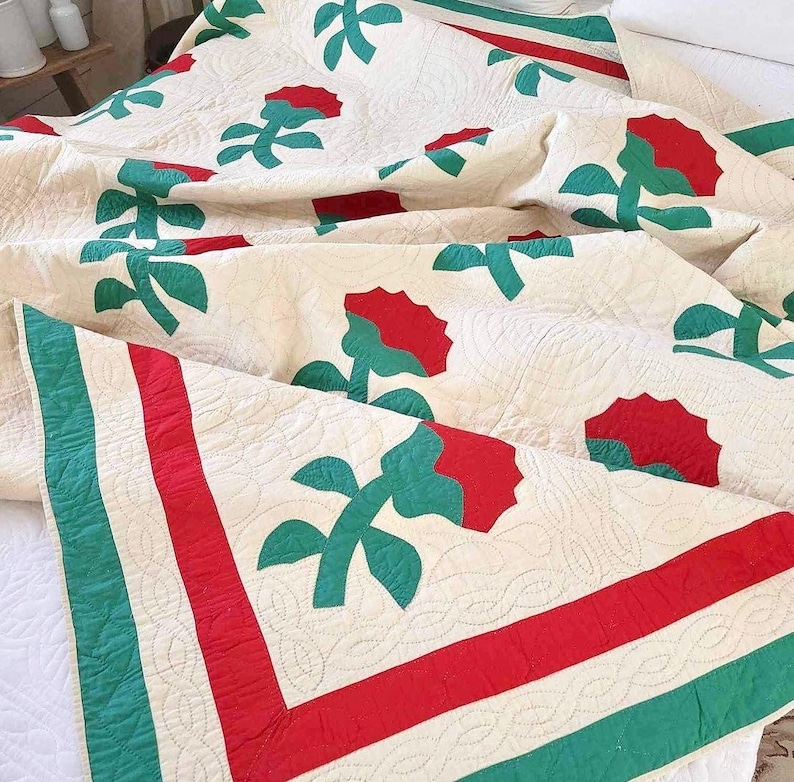 May include: A white quilt with a red and green floral pattern. The quilt has a red and green border.
