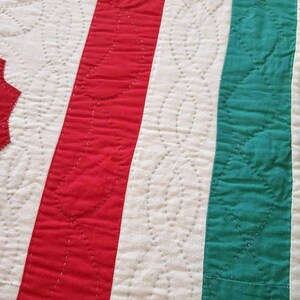 May include: Close-up of a red, white, and green striped fabric with a quilted pattern. The fabric is stitched with a white thread, creating a series of small, curved shapes.
