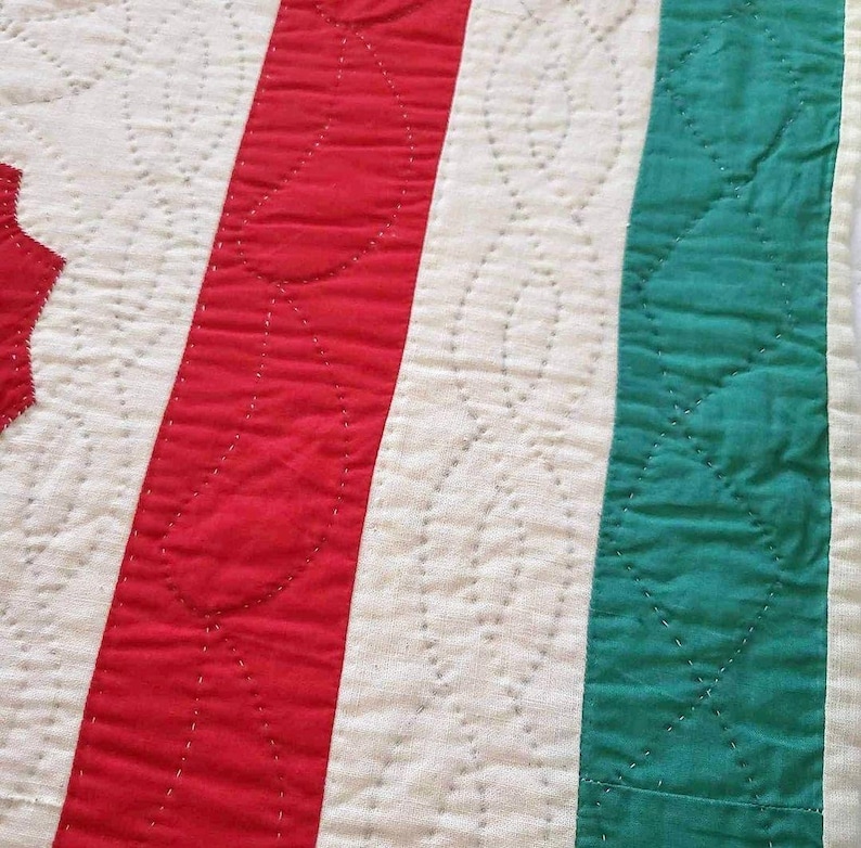 May include: Close-up of a red, white, and green striped fabric with a quilted pattern. The fabric is stitched with a white thread, creating a series of small, curved shapes.