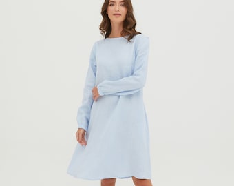 May include: A light blue linen dress with long sleeves and a boat neck. The dress has a relaxed fit and falls to the knee.