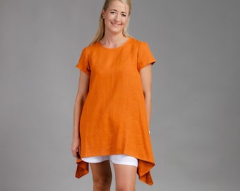 Puede incluir: Una mujer lleva una túnica de lino naranja de manga corta con un dobladillo alto-bajo. También lleva pantalones cortos blancos y sandalias grises.
