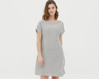 May include: A gray linen dress with a boat neck and short sleeves. The dress has a relaxed fit and falls to the knees.