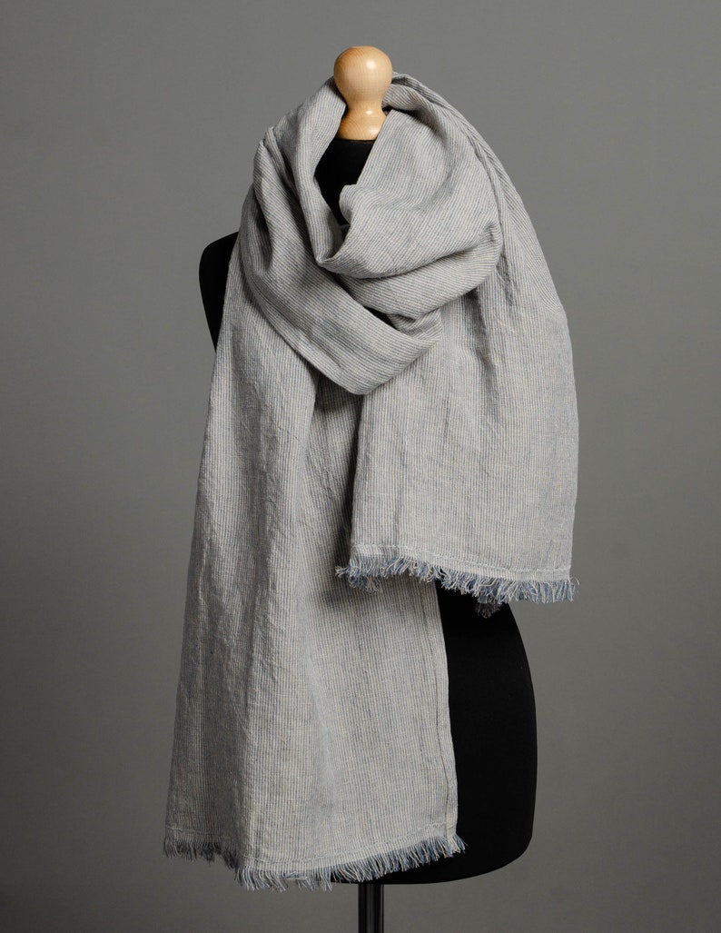May include: A gray and white striped linen scarf with a frayed edge. The scarf is draped over a mannequin.