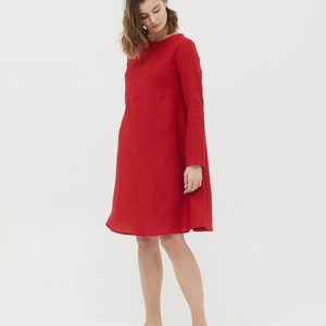 May include: A red linen dress with long sleeves and a slightly flared skirt. The dress is knee-length and has a simple, elegant design.