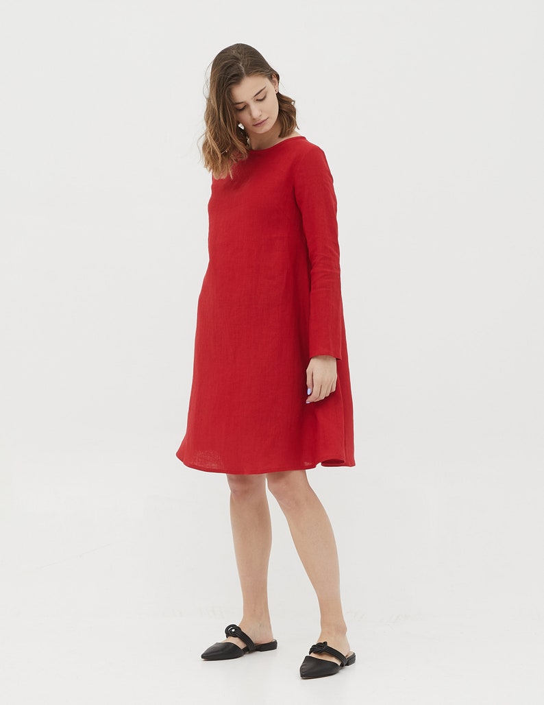 May include: A red linen dress with long sleeves and a slightly flared skirt. The dress is knee-length and has a simple, elegant design.
