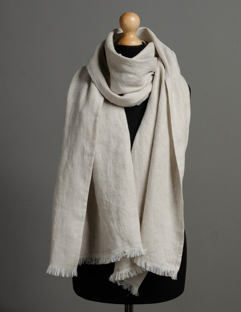 May include: A light beige linen scarf with a fringed edge. The scarf is draped over a mannequin.