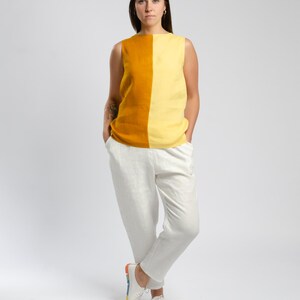 May include: A woman is wearing a sleeveless top with a yellow and orange color block design. She is wearing white pants and white shoes with a rainbow stripe on the sole.