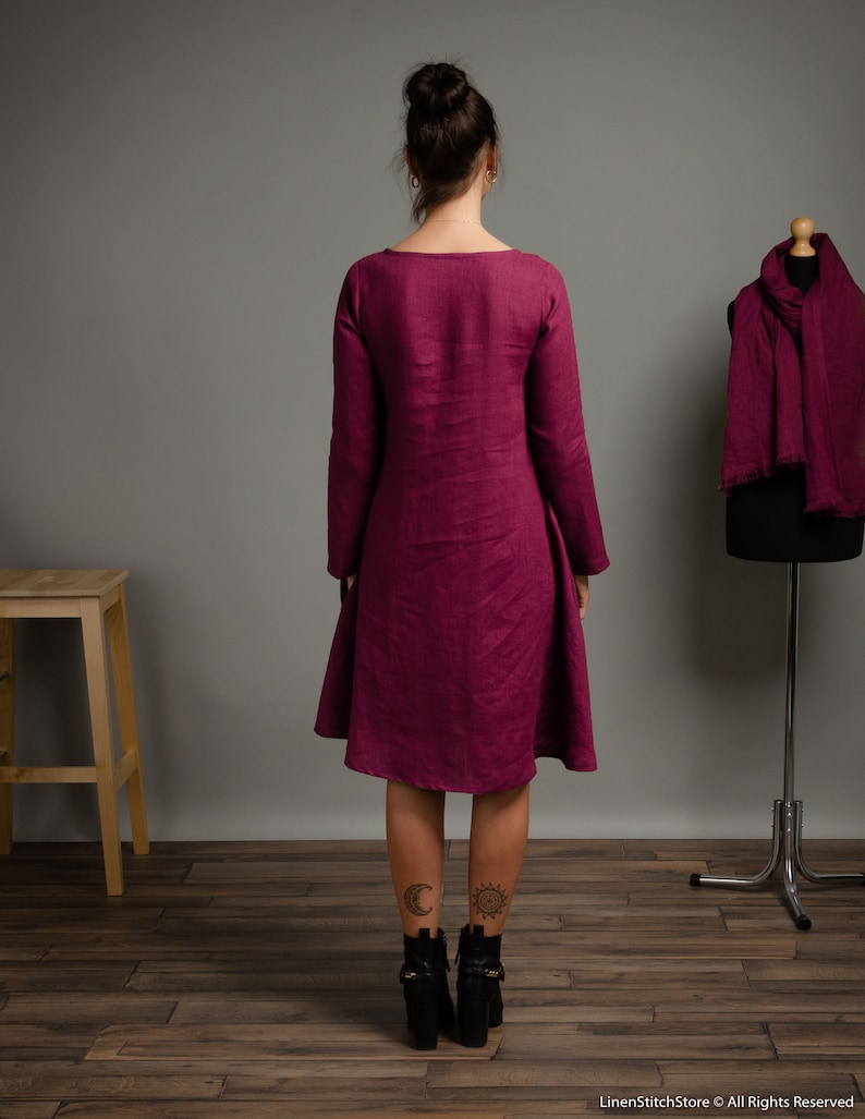 May include: A magenta long-sleeved dress with a round neckline and a flared skirt that falls to the knees. A matching magenta scarf is draped over a dress form standing to the right. The text LinenStitchStore &copy; All Rights Reserved is visible.