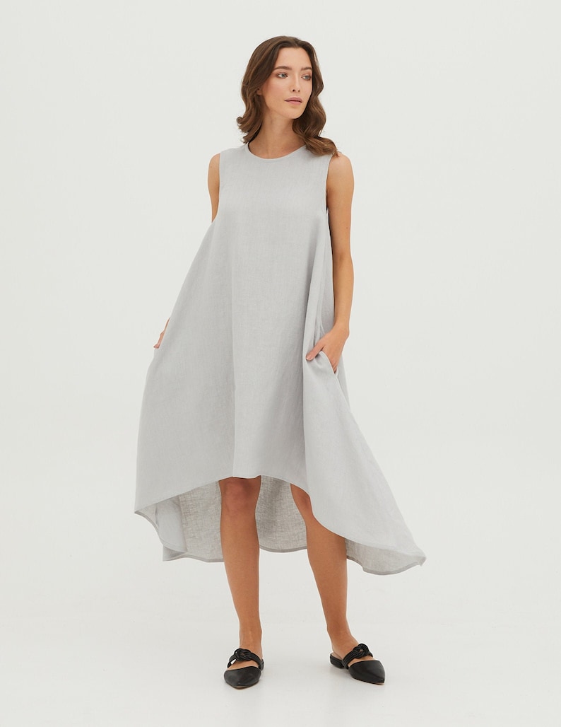 May include: A gray linen dress with a high-low hemline and sleeveless design. The dress has a round neckline and two pockets.