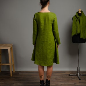 May include: A long-sleeved, green linen dress with a scoop neck and a slightly flared skirt. The dress is shown on a model with black ankle boots.