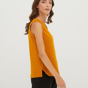 May include: A sleeveless, mustard yellow top with a v-neckline. The top is made of a soft, textured fabric and has a slightly curved hemline.