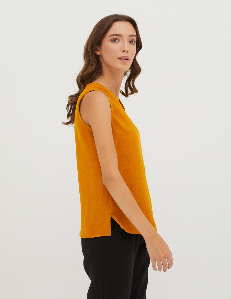 May include: A sleeveless, mustard yellow top with a v-neckline. The top is made of a soft, textured fabric and has a slightly curved hemline.