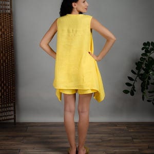 May include: A sleeveless yellow linen dress with a loose fit and a slightly asymmetrical hemline. The dress is paired with matching yellow linen shorts.
