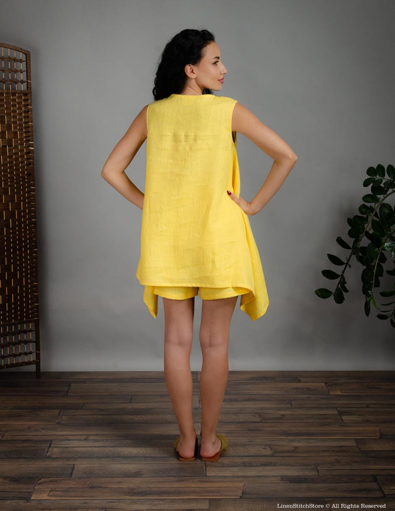 May include: A sleeveless yellow linen dress with a loose fit and a slightly asymmetrical hemline. The dress is paired with matching yellow linen shorts.