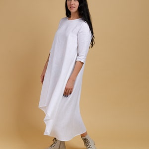 May include: A white linen dress with a long, flowing skirt and three-quarter sleeves. The dress has a simple, elegant design and is perfect for a casual summer outfit.