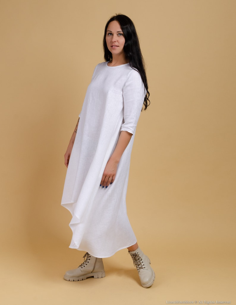 May include: A white linen dress with a long, flowing skirt and three-quarter sleeves. The dress has a simple, elegant design and is perfect for a casual summer outfit.