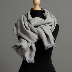 May include: A gray and white striped scarf with frayed edges, draped around a black mannequin.